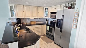 A kitchen with white cabinets, a black countertop, stainless steel appliances, and a tiled floor. - Ocean Block, 2 Bedroom Condo on 37th St. Sovereign Sea. Next to Coconuts Beach Bar and many other great places! Sovereign Sea #302 (Ocean City)
