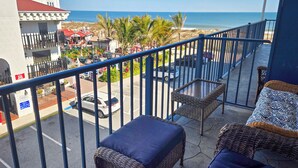 A balcony with wicker furniture, a view of the beach, and a building with a red roof. - Ocean Block, 2 Bedroom Condo on 37th St. Sovereign Sea. Next to Coconuts Beach Bar and many other great places! Sovereign Sea #302 (Ocean City)