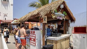 A beachside kiosk with a thatched roof, a sign reading "Coconut Bar," and a sign indicating a wristband is required for alcoholic beverages. - Ocean Block, 2 Bedroom Condo on 37th St. Sovereign Sea. Next to Coconuts Beach Bar and many other great places! Sovereign Sea #302 (Ocean City)