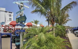 A beachside market with directional signs, palm trees, and outdoor seating areas.
