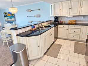 A kitchen with white cabinetry, a black countertop, a coffee maker, and a trash can.