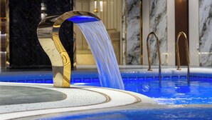 A luxurious indoor pool with a modern water feature, marble walls, and elegant lighting. - Bogishamol Hotel (Samarkand)