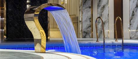 Una piscina interior lujosa con un moderno elemento acuático, paredes de mármol e iluminación elegante.