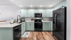 Een moderne keuken met lichtgroene kastjes, roestvrijstalen apparatuur en een houten vloer.