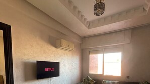 Sala de estar com televisão de tela plana na parede, sofá, mesa de centro e janela que proporciona iluminação natural.