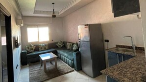 Uma sala de estar moderna com sofá, mesa de centro e área de cozinha com geladeira e pia.