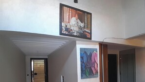 Um corredor iluminado por uma luminária no teto, com uma porta no final e um quadro na parede.
