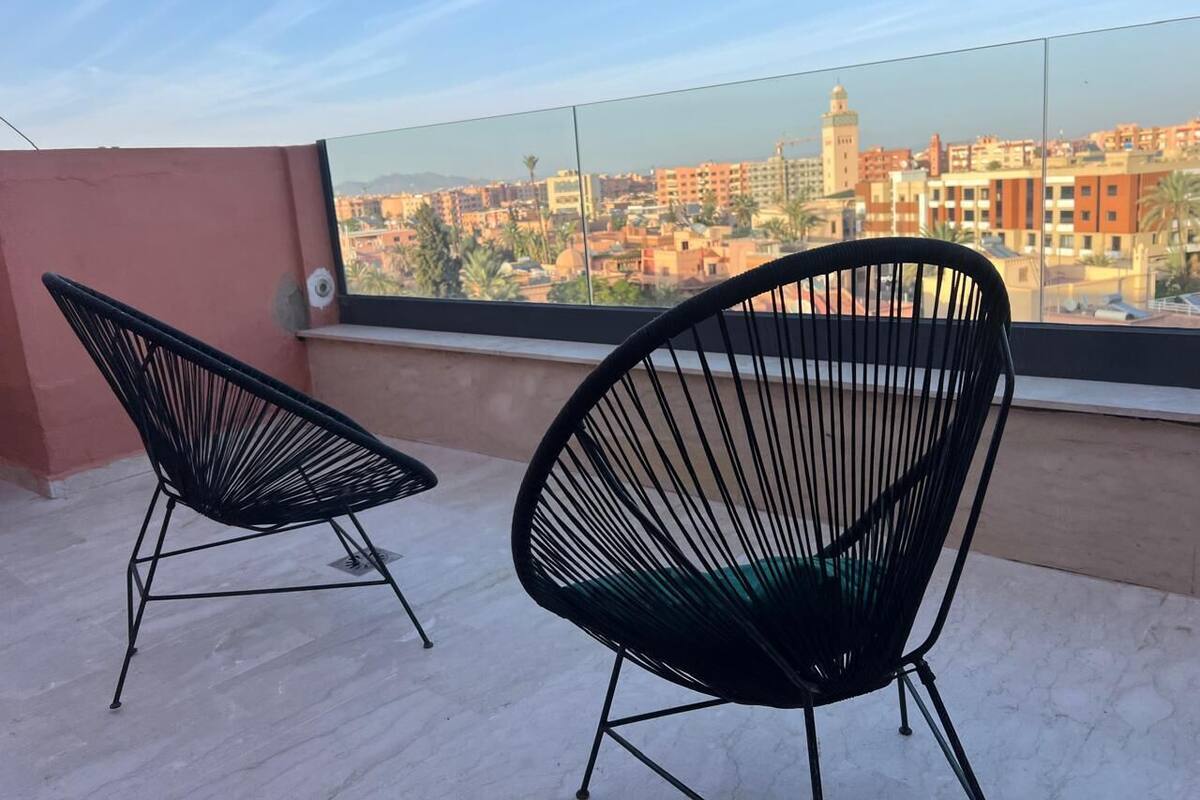 Two black wireframe chairs on a balcony with a cityscape view.