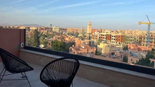 Uma varanda com duas cadeiras pretas, com vista para um horizonte urbano com edifícios e uma grua de construção.