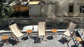 A rooftop terrace with outdoor seating and a view of a building with a red-tiled roof. - Mykonos Hotel (Odesa)