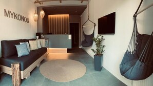 A modern living room with a sofa, hanging chairs, a potted plant, and a TV mounted on the wall. - Mykonos Hotel (Odesa)