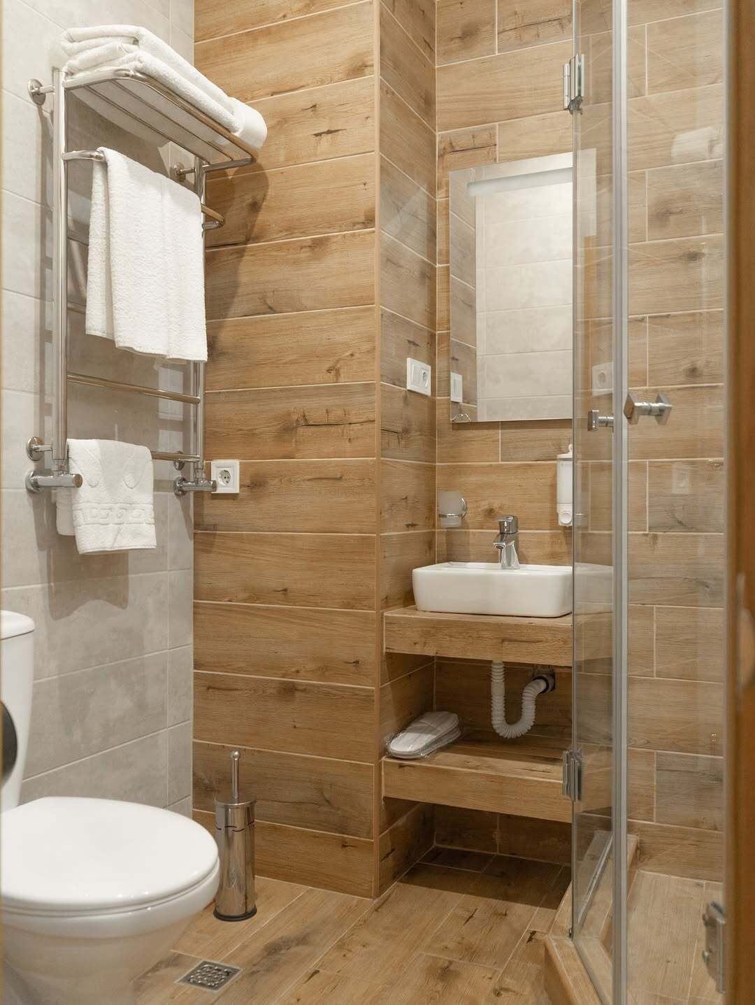 Un baño moderno con diseño de paneles de madera, cabina de ducha de vidrio, lavabo blanco y un inodoro.