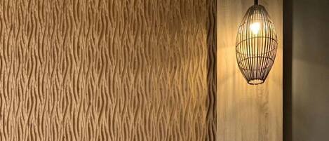Un lit bien fait, avec un ordinateur portable posé dessus, une table de chevet avec une lampe et un mur à la texture intéressante.