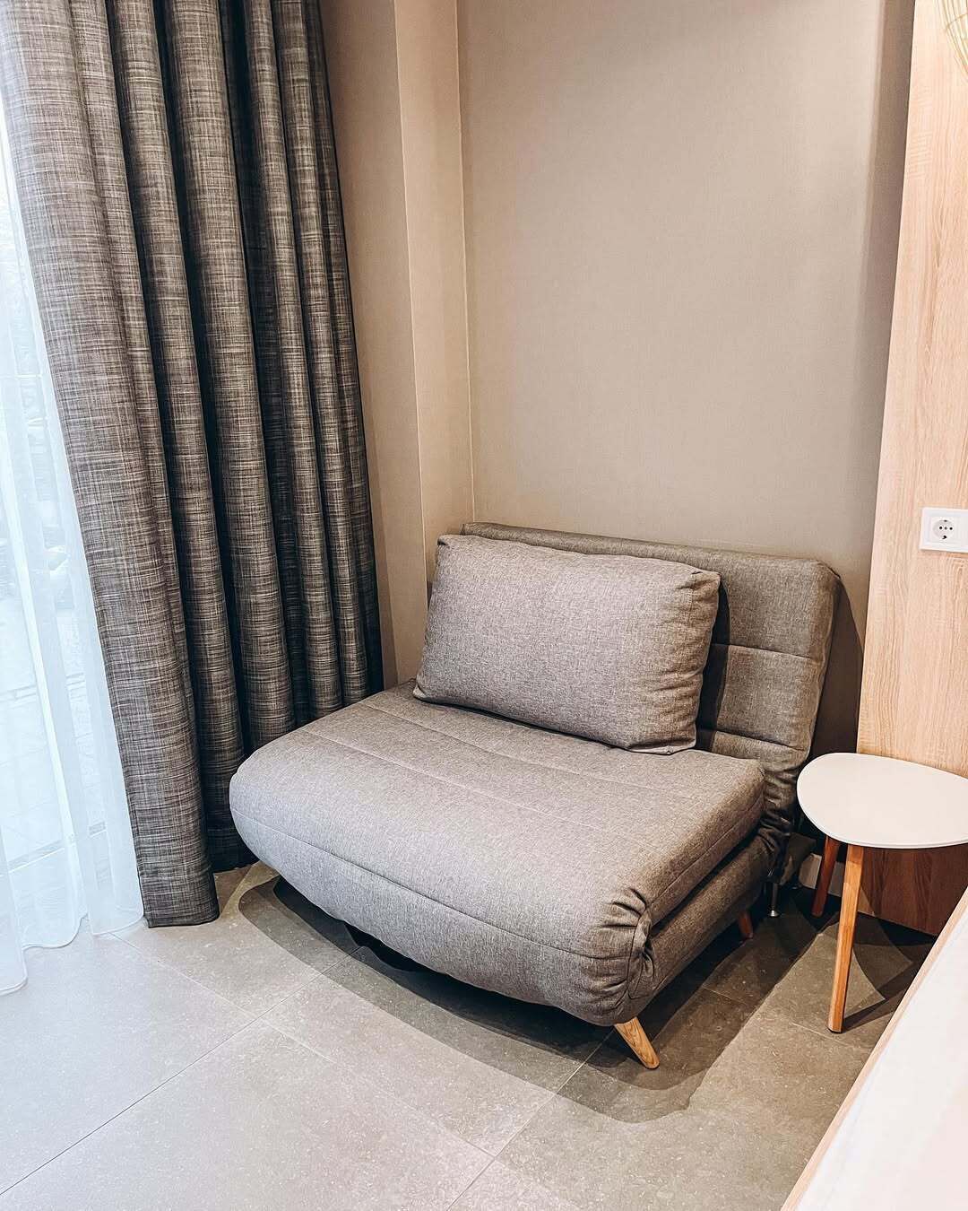A corner sofa with a matching pillow, a small round table, and a power outlet on the wall.