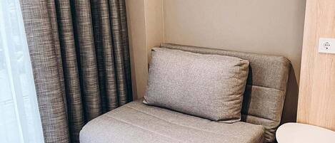 A corner sofa with a matching pillow, a small round table, and a power outlet on the wall.