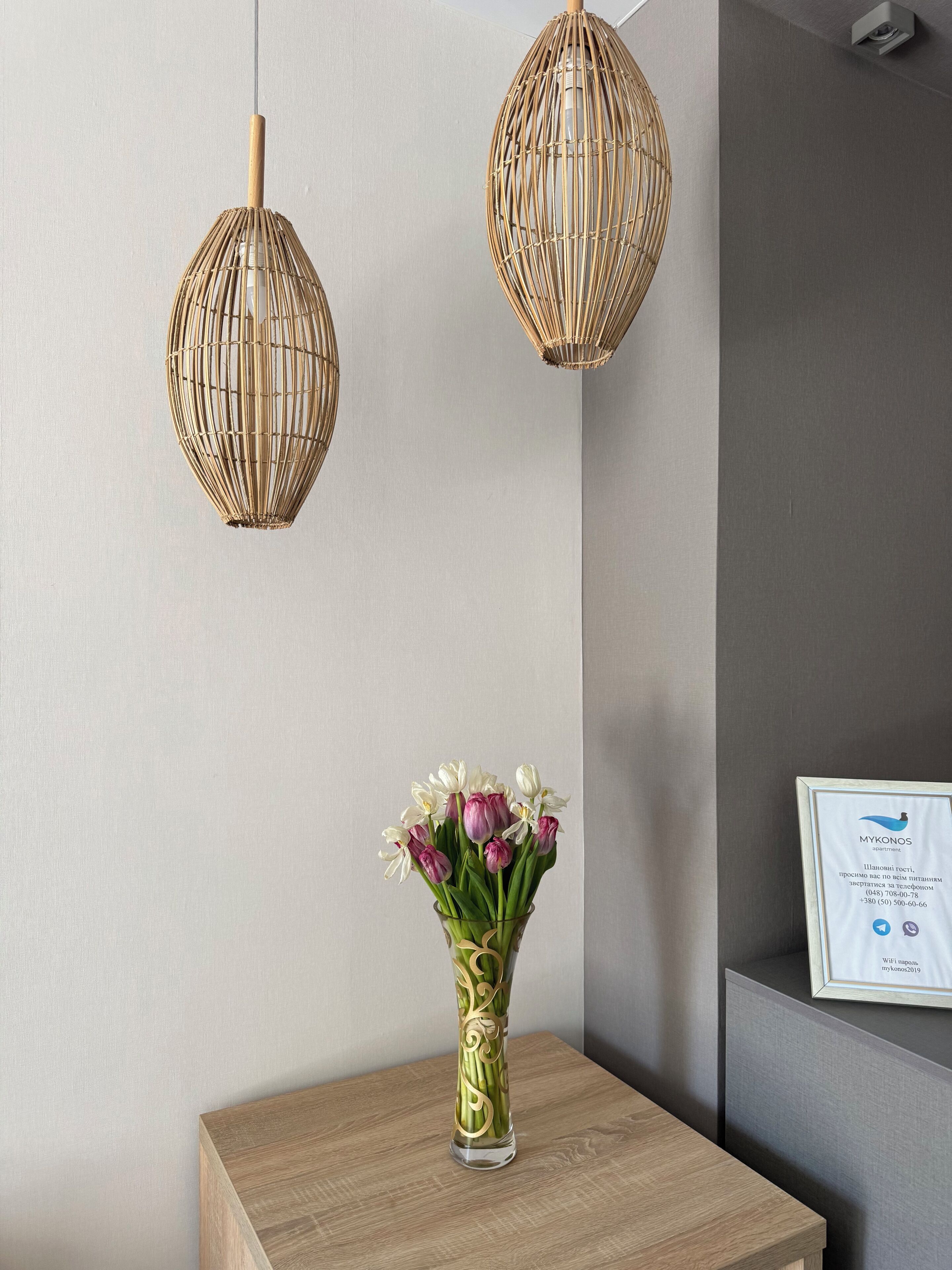 A reception area with a wooden table, a vase of flowers, and two wicker pendant lights.