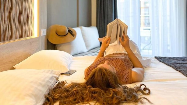 A hotel room with a bed, a reading lamp, a wall-mounted air conditioner, and a window with curtains. - Mykonos Hotel (Odesa)