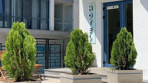 A hotel named 'Mikonos' with a modern facade, large windows, and three potted evergreen trees in front. - Mykonos Hotel (Odesa)