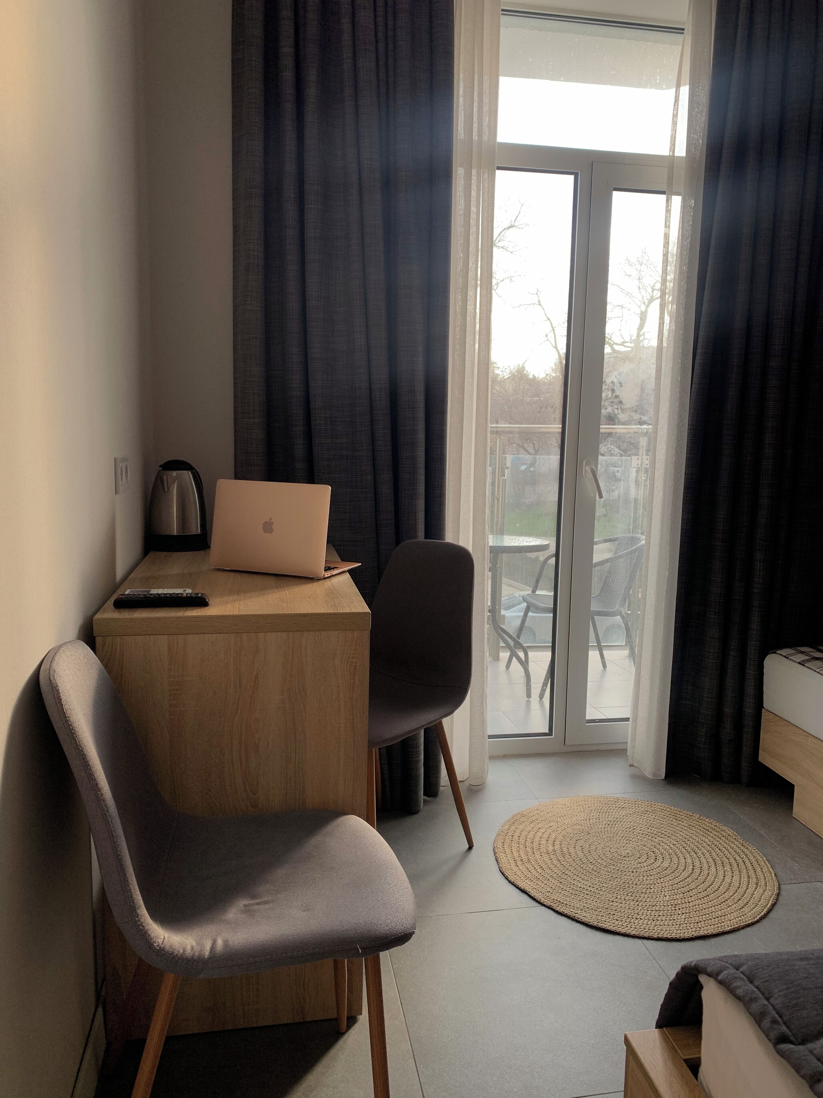 Een moderne kamer met een houten bureau, een laptop, een stoel, een bed en uitzicht door een glazen deur op een buitenruimte.