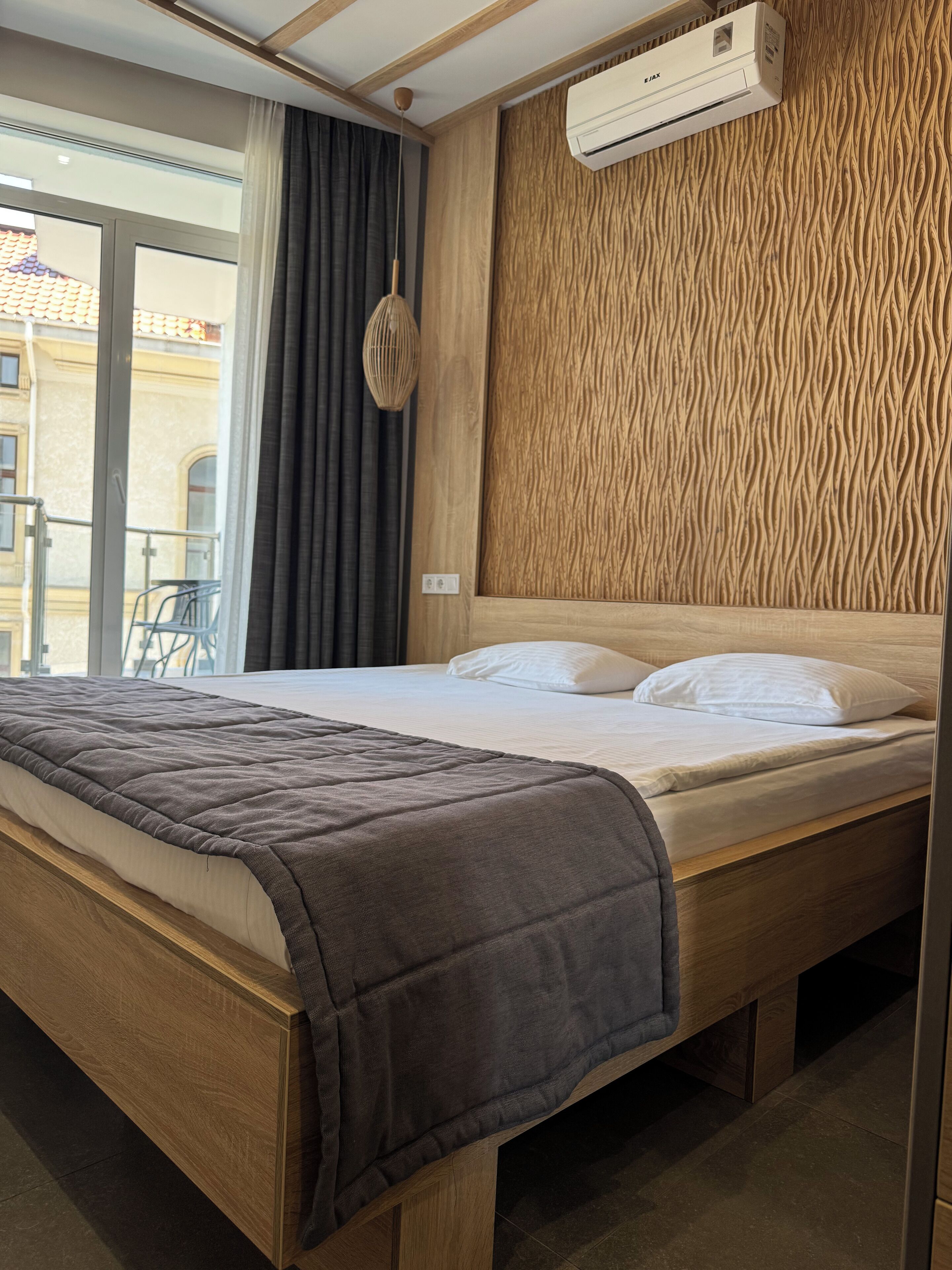 Une chambre d’hôtel avec un lit en bois, une grande fenêtre et un climatiseur fixé au mur.