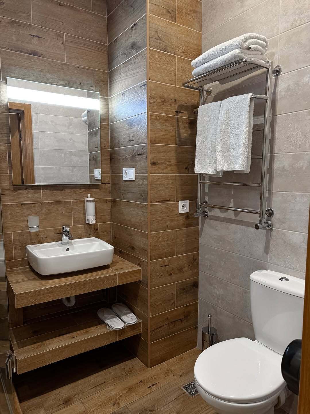 A modern bathroom with a wooden vanity, a white sink, a towel rack, and a toilet.