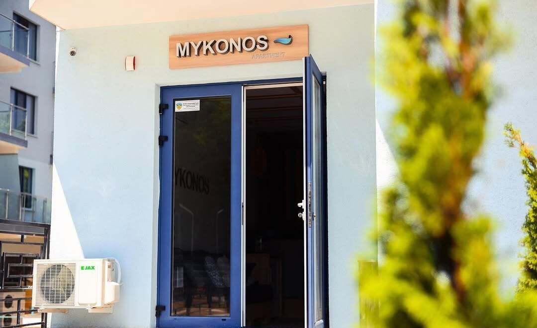 A building with a blue door and a sign that reads "MYKONOS".