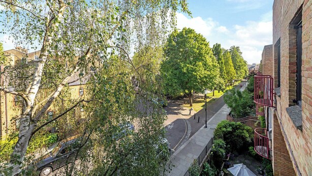Une rue étroite bordée d’arbres, avec un bâtiment en briques d’un côté.