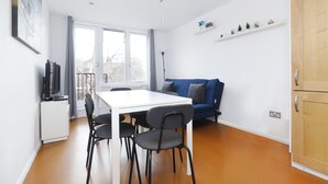 Un salon moderne avec une table à manger blanche, des chaises noires, un canapé bleu et un téléviseur posé sur un meuble blanc.