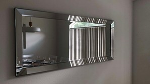 Ein großer, rechteckiger Spiegel mit Metallrahmen an einer schlichten Wand befestigt.