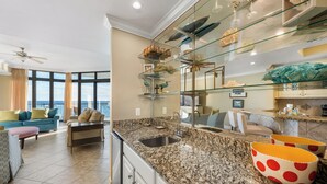 A modern kitchen with granite countertops, a built-in sink, and a glass display shelf with decorative items. - The Oasis at Orange Beach 1102 (Orange Beach)
