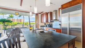 A modern kitchen with a large island, stainless steel appliances, and a view of a tropical landscape.