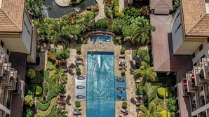An aerial view of a hotel with a central swimming pool surrounded by lush landscaping and multiple balconies.