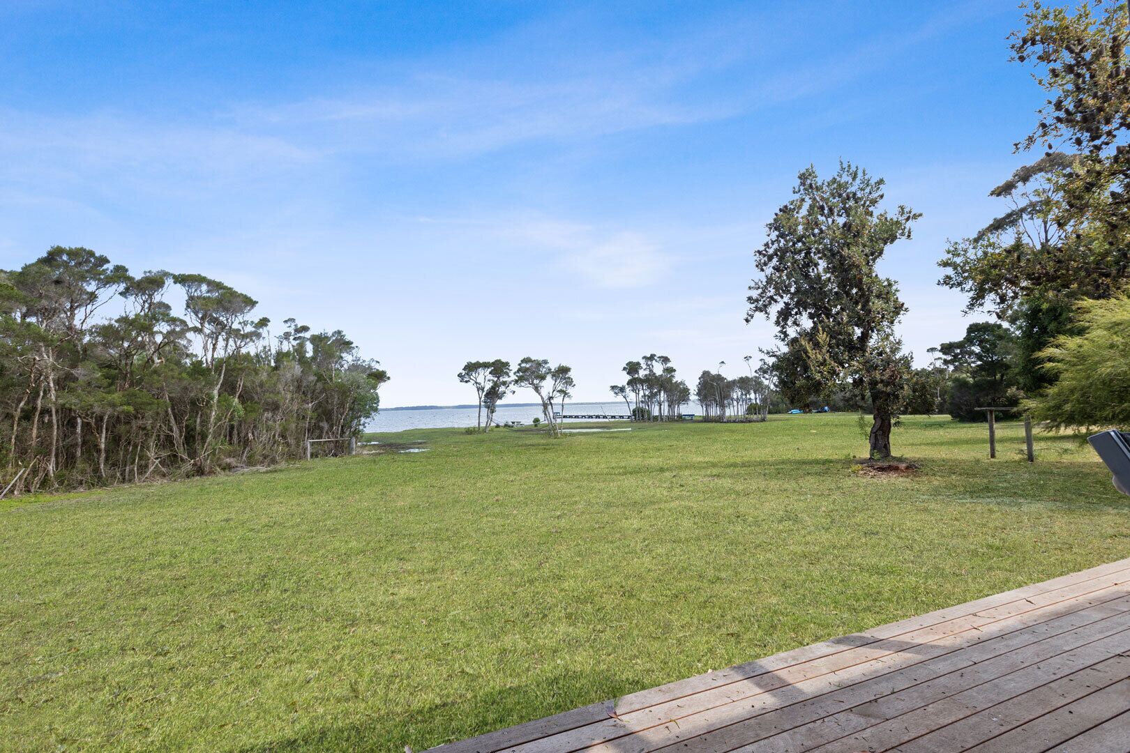 Un espacio al aire libre con césped, una terraza de madera, árboles y vista al agua.
