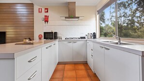 A modern kitchen with white cabinetry, a gas stove, a microwave, and a large window offering a view of trees. - Dargo - Waterfront Retreat: Secluded lodges perfect for nature lovers (Forge Creek)