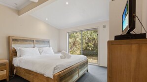 A bedroom with a wooden bed, a nightstand, a TV on a stand, and a sliding glass door to the outdoors. - Dargo - Waterfront Retreat: Secluded lodges perfect for nature lovers (Forge Creek)