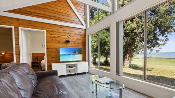 Una sala de estar moderna con techo de madera, un televisor grande en la pared, una mesa de centro de vidrio y vistas al exterior.