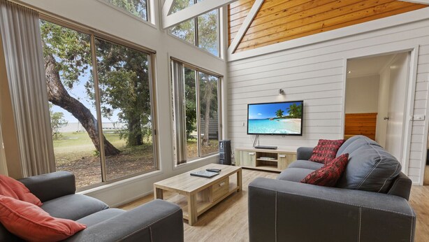 A modern living room with a large TV, grey sofas, and a wooden coffee table. - Westwind - Waterfront Retreat: Secluded lodges perfect for nature lovers (Forge Creek)