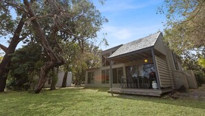 A small, single-story house with a sloped roof and large windows, surrounded by a grassy yard and trees. - Westwind - Waterfront Retreat: Secluded lodges perfect for nature lovers (Forge Creek)