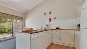 Une cuisine moderne avec des armoires blanches, un plan de travail en bois et un lave-vaisselle encastré. Trois panneaux rouges indiquant les consignes de sécurité incendie sont accrochés au mur.