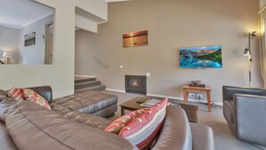 Un salon moderne doté d’un grand canapé d’angle, d’une cheminée et d’un téléviseur à écran plat fixé au mur.