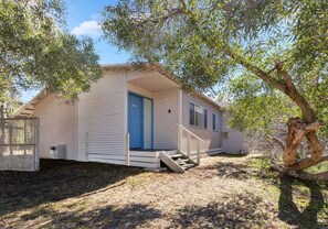 A single-story mobile home with a blue door, a small porch, and a staircase leading to the entrance.