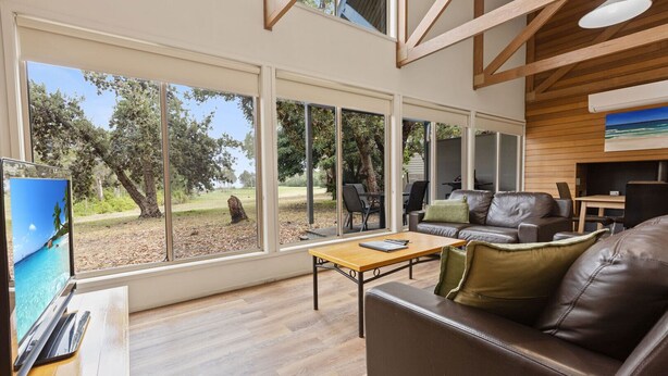 Un salon spacieux doté de grandes fenêtres, d’un canapé en cuir, d’une table basse en bois et d’un téléviseur.