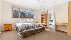 Un dormitorio con cama, escritorio, armario y ventana con vistas a árboles.