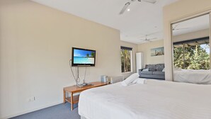 A modern hotel room with a large bed, a television mounted on the wall, a grey sofa, and a large window offering a view of trees. - Secluded lodges perfect for nature lovers (Forge Creek)