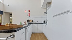 A modern kitchen with white cabinets, a black countertop, and a wooden floor. There are fire safety signs on the wall and a window providing natural light. - Secluded lodges perfect for nature lovers (Forge Creek)