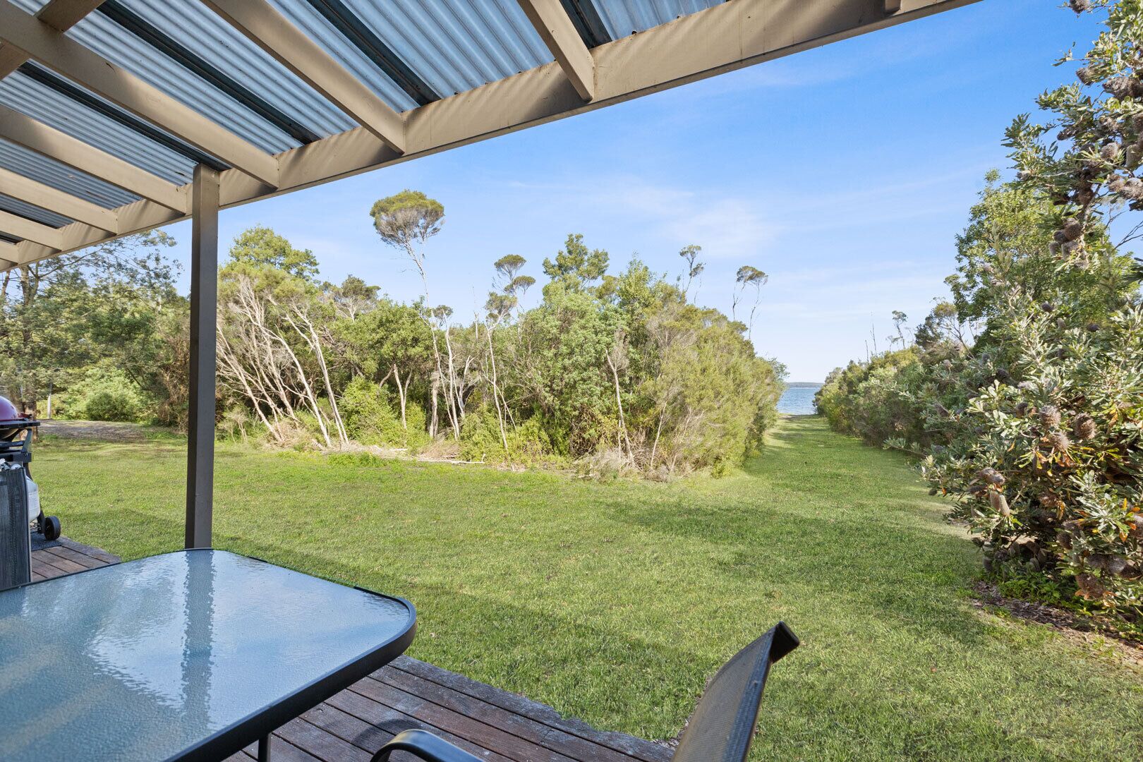 A covered outdoor area with a table and chairs, surrounded by a grassy lawn and trees.