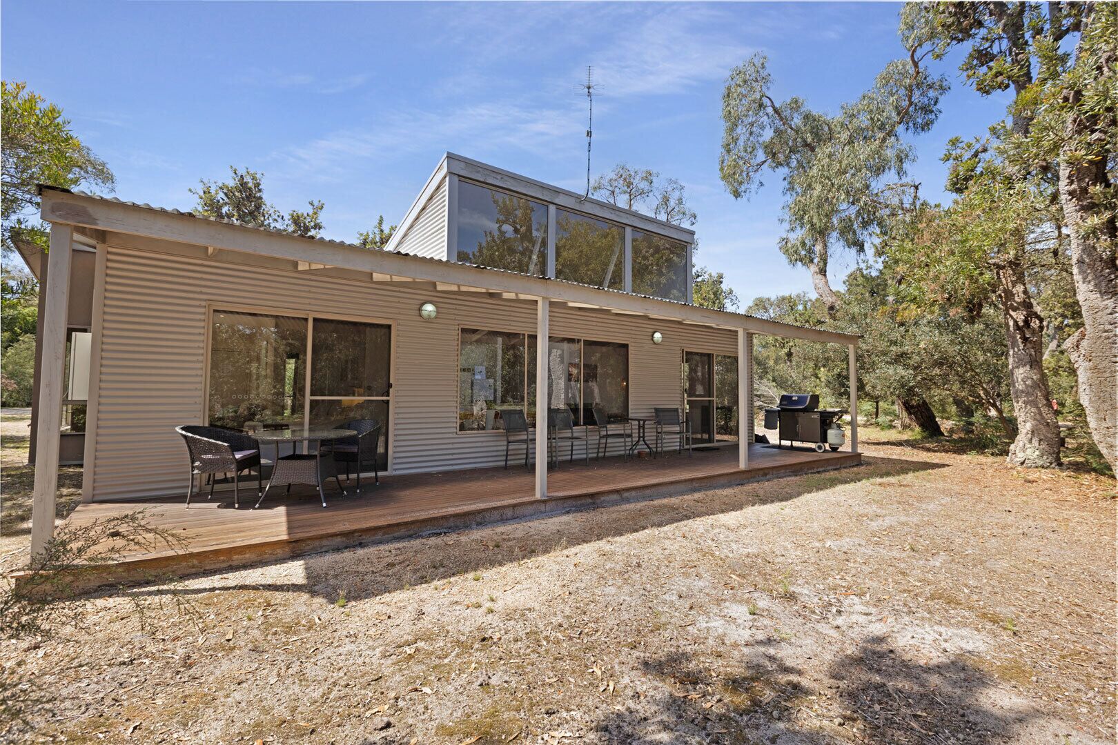 Ein modernes Haus mit überdachter Terrasse, großen Fenstern und Grillplatz.