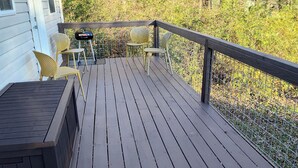 A wooden deck with a railing, a grill, and two chairs.