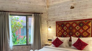 Habitación de hotel con techo de madera, una cama grande con ropa blanca, almohadas rojas y blancas, y vista a zonas verdes.