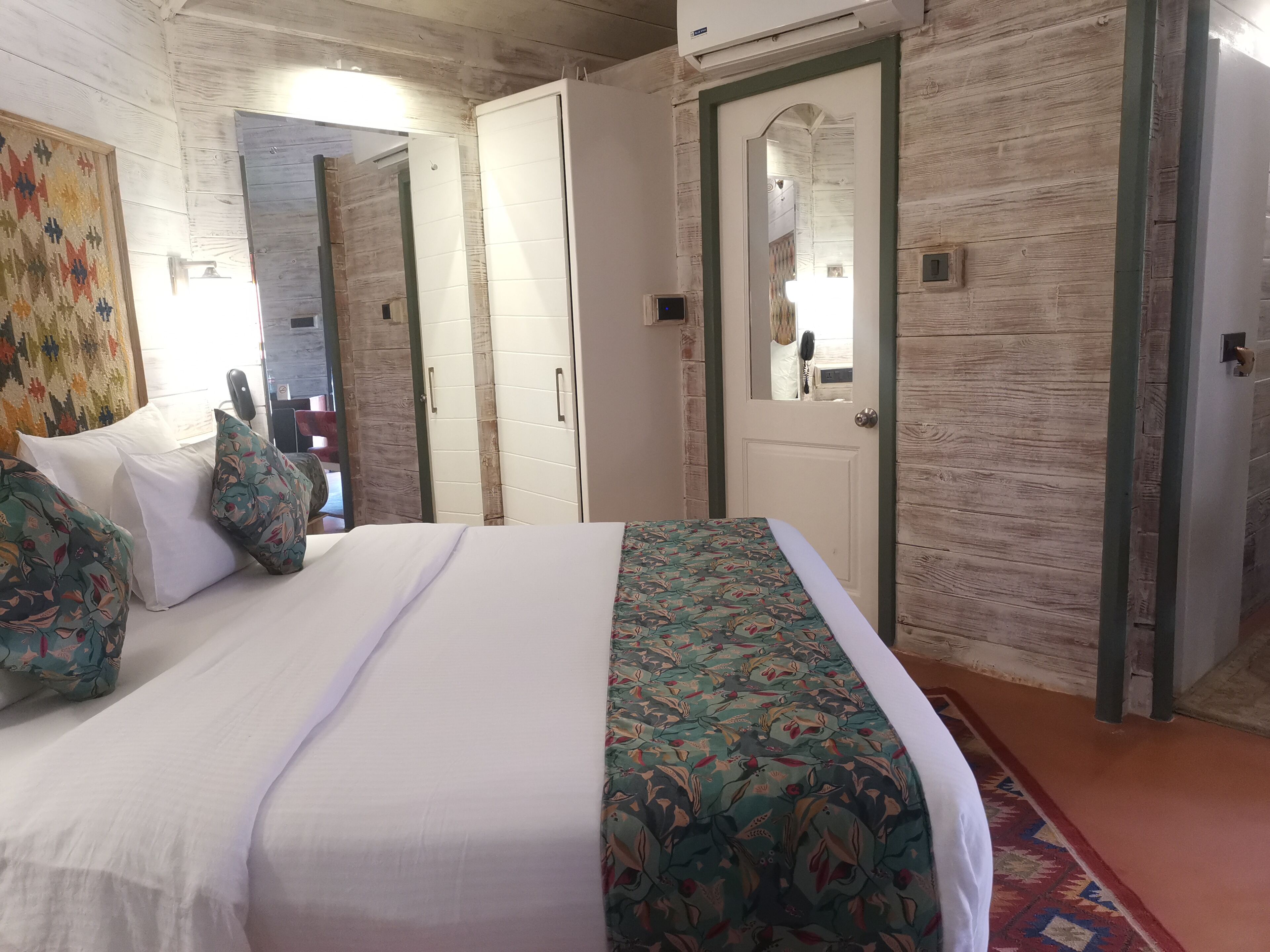 A bedroom with a bed, pillows, a mirror, and a door.